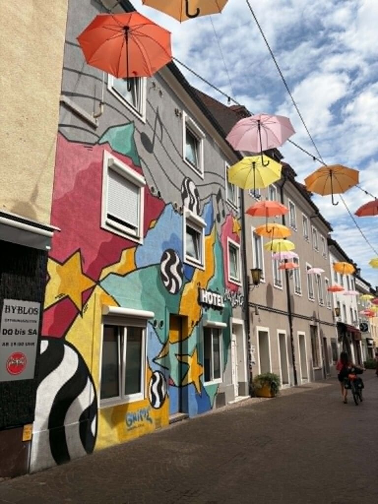 Villach arcai: a nyugodt Drau-part és a vidám, színes ernyőkkel díszített belvárosi utca.