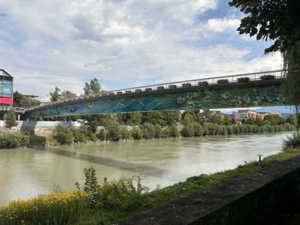 Villach arcai: a nyugodt Drau-part és a vidám, színes ernyőkkel díszített belvárosi utca.
